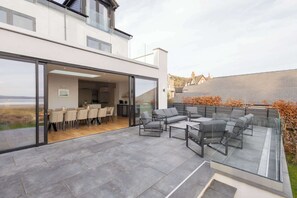 A modern house with a glass-enclosed dining area, a patio with outdoor furniture, and a view of the countryside. - Host & Stay | Bay View House (Grange-over-Sands)