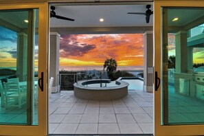 A modern outdoor pool area with a circular water feature, surrounded by white chairs, and a view of the sunset over the ocean. - Beautiful New Beach Home with Private Pool, Spa & Stunning Beach Views (Hilton Head Island)
