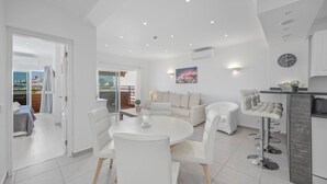 Un salon moderne avec un canapé blanc, une table de salle à manger ronde et un coin cuisine doté d’un bar.