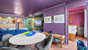 A modern room with a purple wall, a wooden bed, a blue sofa, and a dining table with chairs.