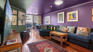 A modern living room with a blue sofa, wooden coffee table, and a red patterned rug.