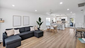 Un salon moderne avec un canapé d’angle, un coin repas et une cuisine en arrière-plan.