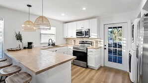 Une cuisine moderne avec des meubles blancs, un grand îlot central doté de tabourets, des appareils en acier inoxydable et un éclairage suspendu.