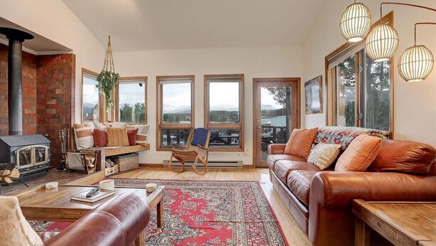A cozy living room with a fireplace, leather sofa, and large windows offering a view of the mountains.