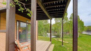 A covered outdoor area with a wooden deck, a glass door leading inside, and a view of a pond and trees in the background.