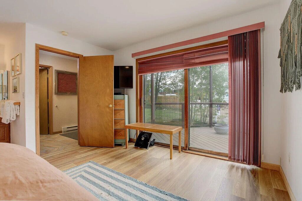 A room with a wooden floor, a bench, a sliding glass door to a deck, and a television on the wall.
