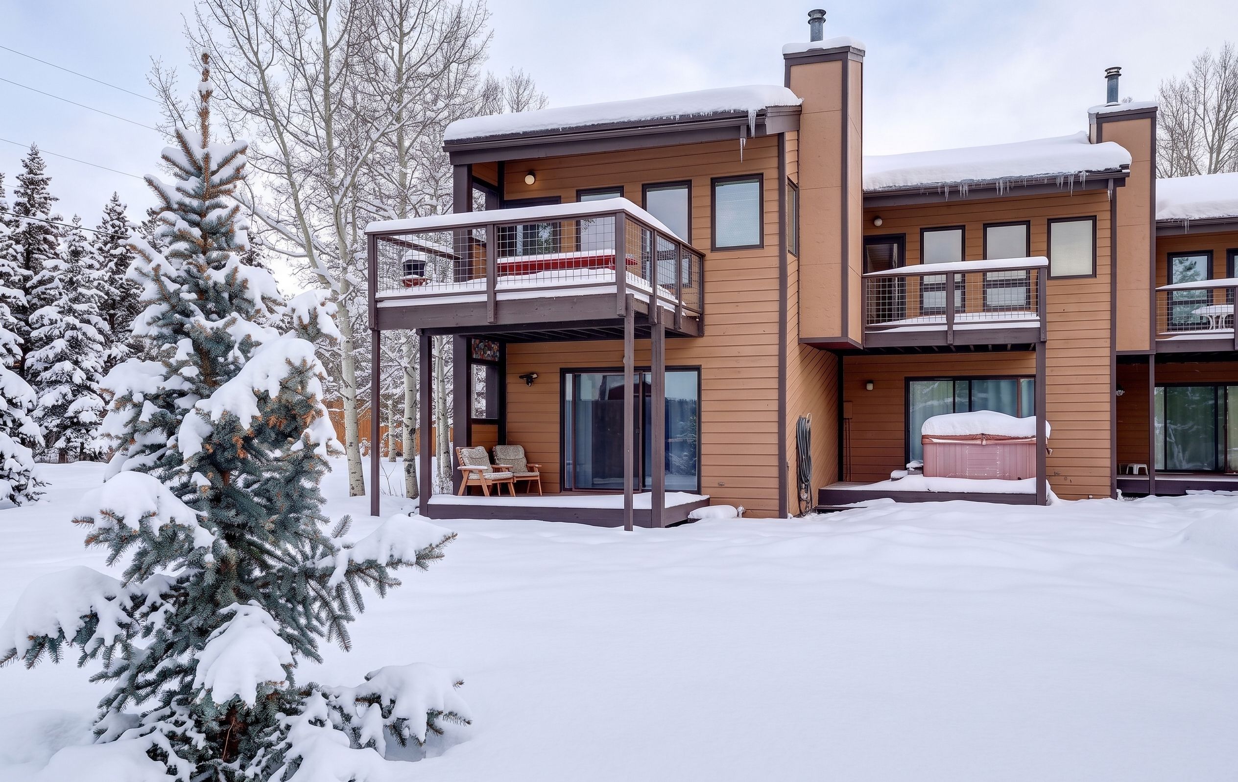 Enjoy a serene winter retreat! This inviting townhome features excellent outdoor living spaces, including a covered hot tub and private decks, all surrounded by a beautiful snow-blanketed yard and mature pine trees