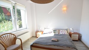 Una camera da letto con un letto, comodini, una sedia e una finestra vista verde.
