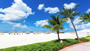 A beach with white sand, palm trees, and thatched-roof huts. - Lely, Naples home with The Players Club at Lely Resort Amenities (Naples)