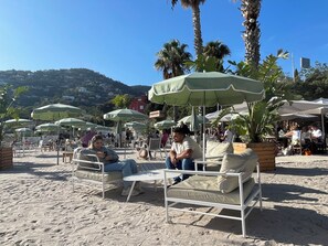 Outdoor seating with umbrellas, a sandy beach, and palm trees.