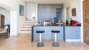 A modern kitchen with a central island, two bar stools, and a staircase leading to another level. - Enchanting beach house in Théoule-sur-Mer directly on the Plage de la Figueirette (Théoule-sur-Mer)