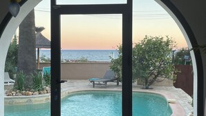 A pool area with a view of the sea at sunset, a covered seating area, and a stone-tiled deck. - Enchanting beach house in Théoule-sur-Mer directly on the Plage de la Figueirette (Théoule-sur-Mer)