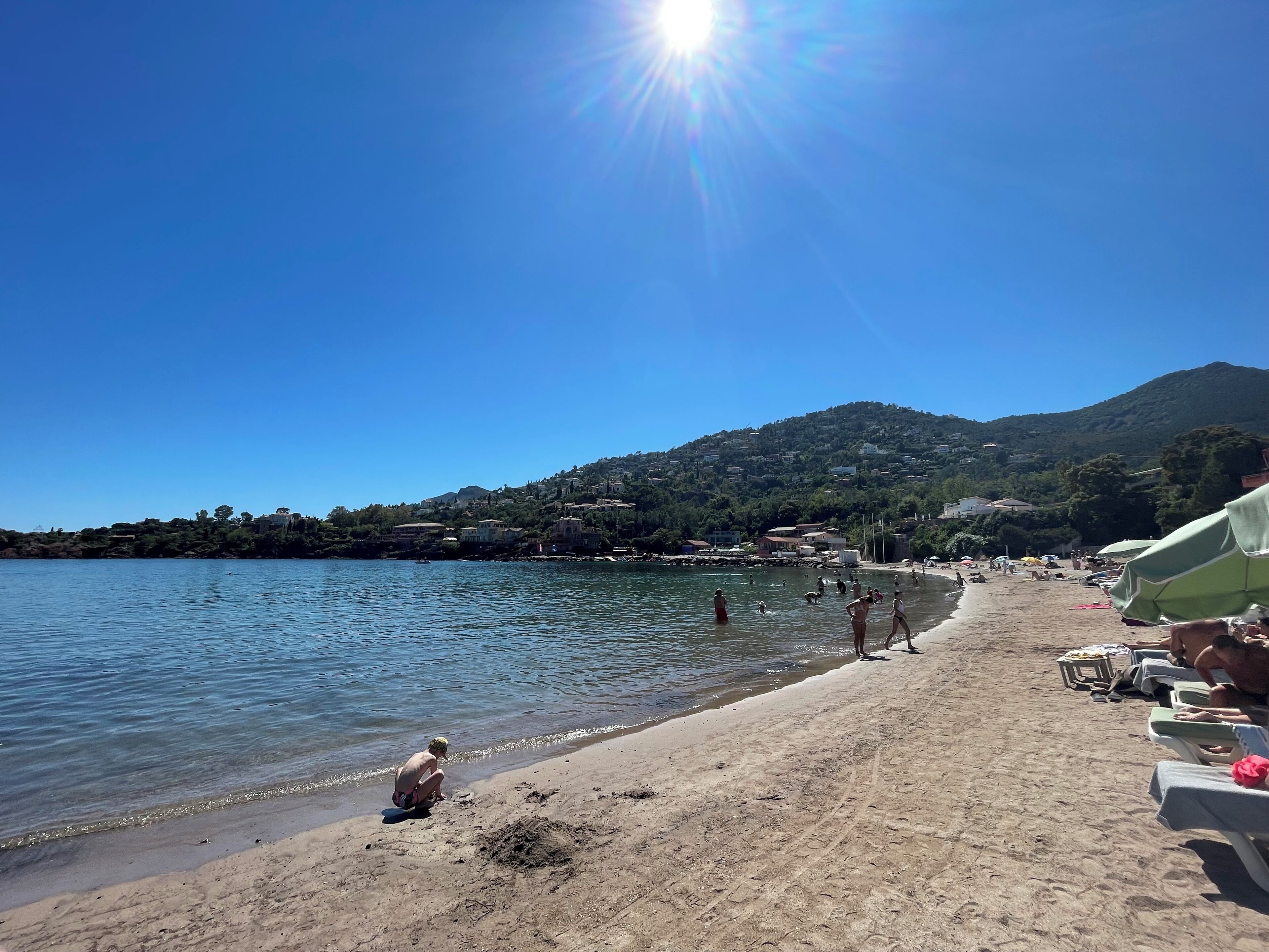 A beach with clear skies, a calm sea, and a mountainous backdrop.
