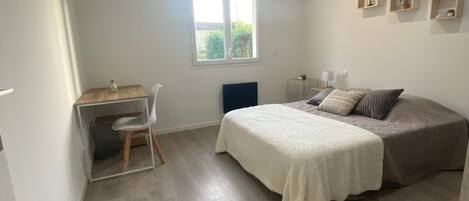 Un dormitorio con cama, escritorio y silla. Se ve un ventanal con vistas a zonas verdes.
