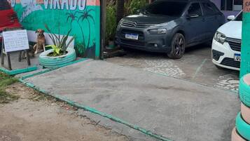 Un área de estacionamiento con un auto Volkswagen y una camioneta SUV gris. Hay neumáticos usados como macetas con plantas. Se observa un letrero en el fondo.