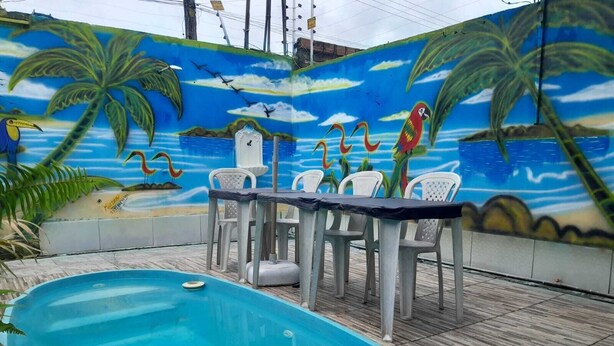 A swimming pool with a mural, a table with chairs, and a wooden deck. - Hospedagem Chapéu Virado  (Belém)