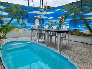 A swimming pool with a mural, a table with chairs, and a wooden deck. - Hospedagem Chapéu Virado  (Belém)