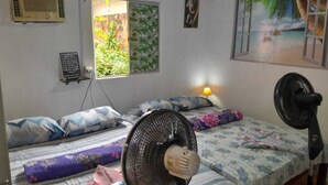 A bedroom with two beds, a standing fan, a wall-mounted heater, a window with a view of greenery, and a painting on the wall. - Hospedagem Chapéu Virado  (Belém)