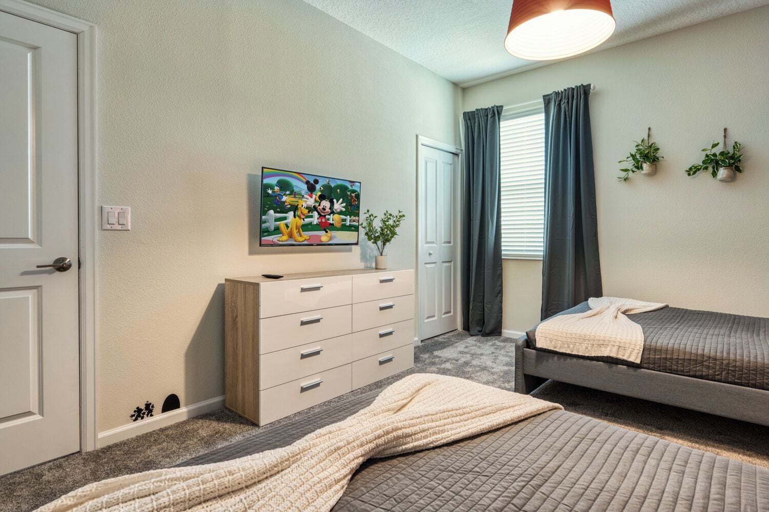 A bedroom with two beds, a dresser, a television, and a window with curtains.