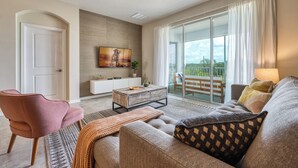 A modern living room with a sofa, armchair, coffee table, and a TV mounted on the wall. - Champions Gate condos by UNE (Davenport)
