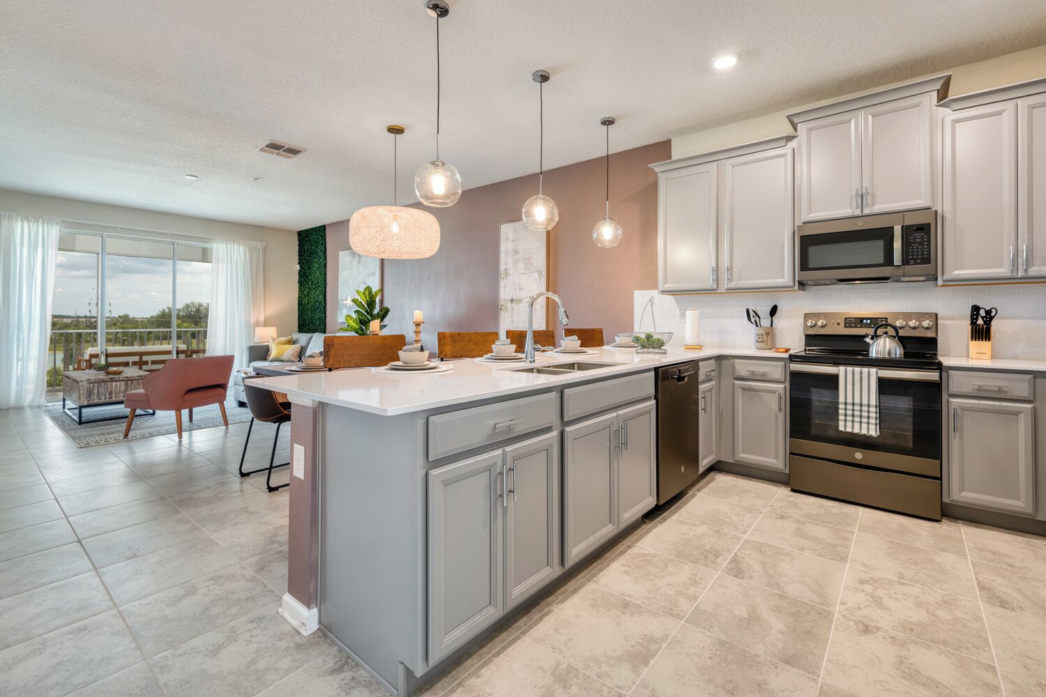 A modern kitchen with grey cabinets, stainless steel appliances, and pendant lighting.