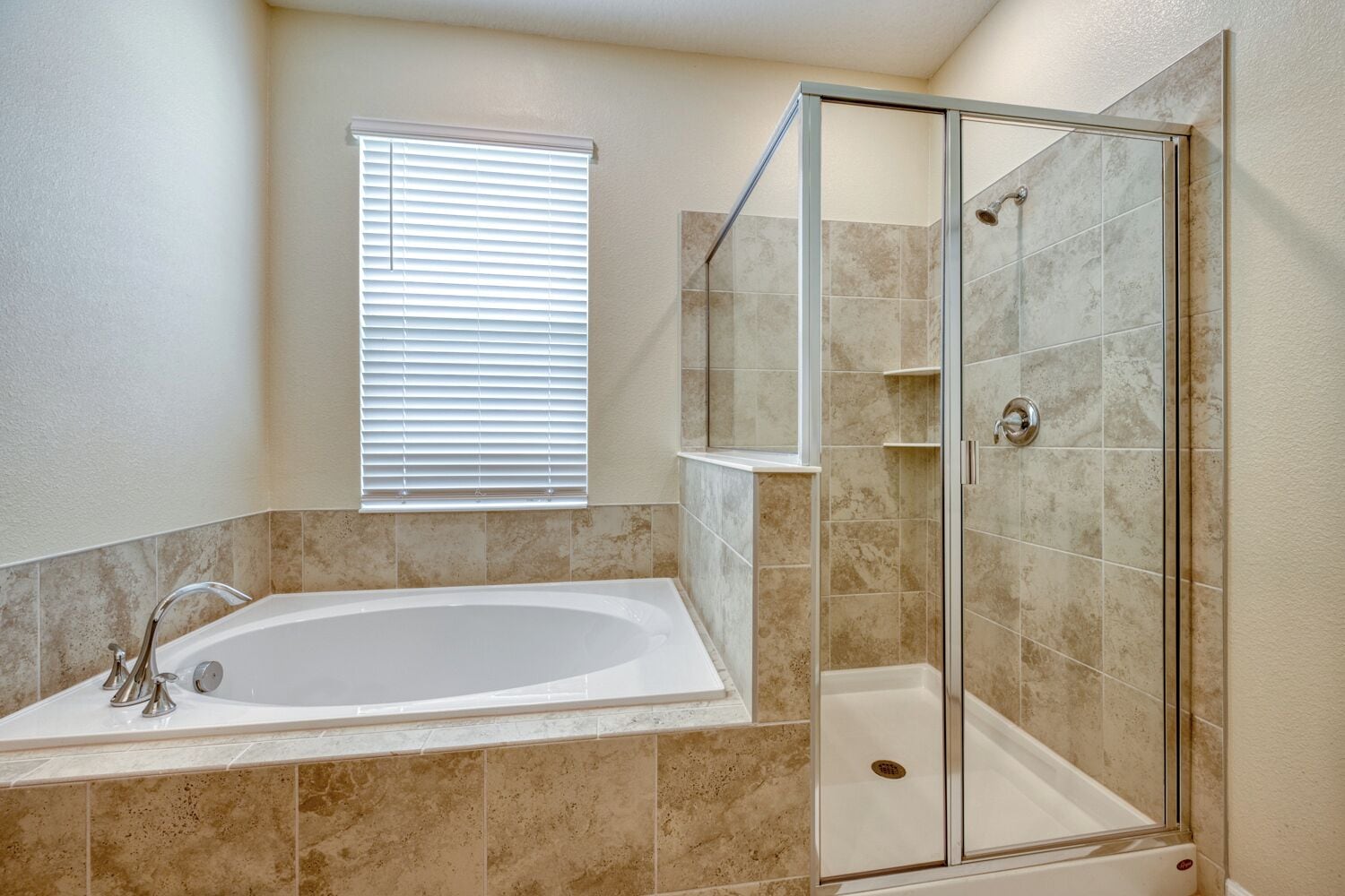 A bathroom with a bathtub, a glass shower enclosure, and a window with blinds.