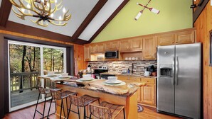 Una cocina moderna con una isla grande, armarios de madera, un refrigerador de acero inoxidable y vistas al exterior.