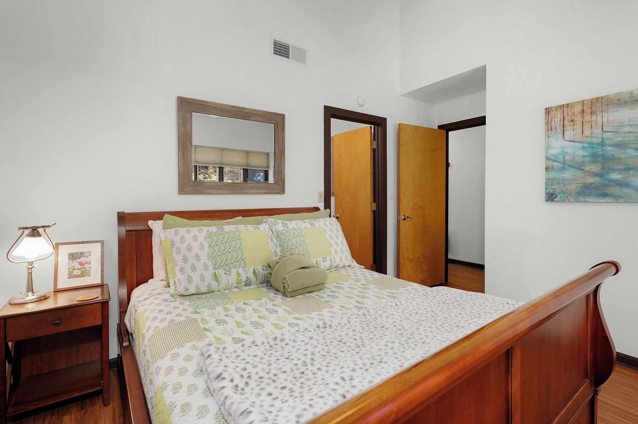 A neatly made bed with a patterned bedspread, a bedside lamp, and a framed picture on a wooden nightstand.