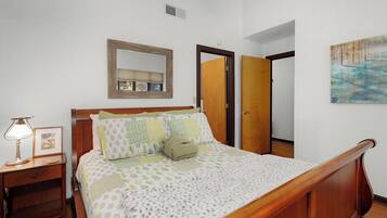 A neatly made bed with a patterned bedspread, a bedside lamp, and a framed picture on a wooden nightstand.
