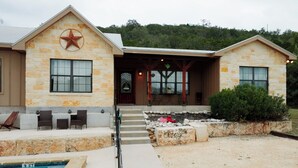A two-story stone house with a pool, outdoor seating, and a star emblem on the facade.