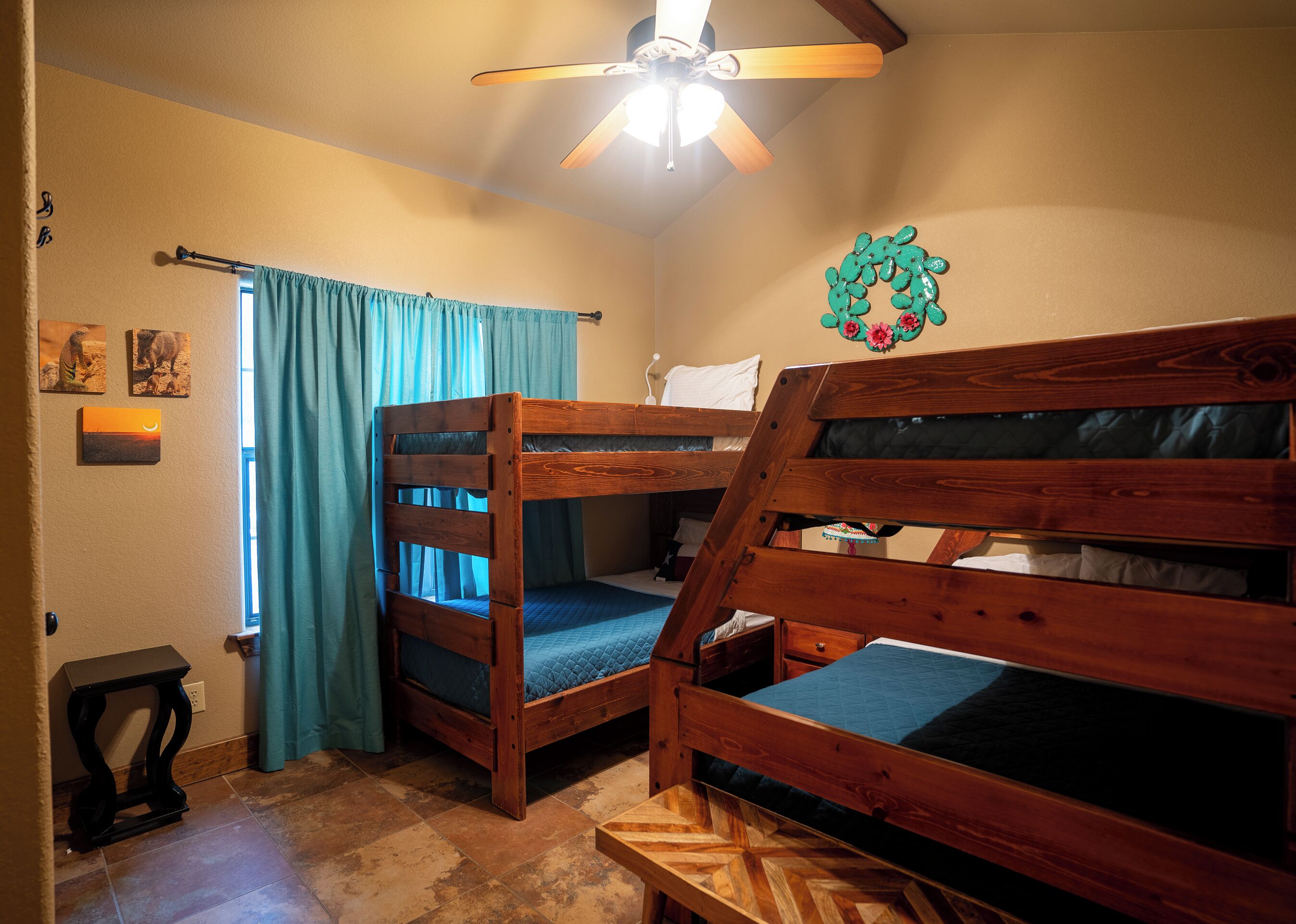A room with two bunk beds, a ceiling fan, a window with curtains, and a wall decoration.