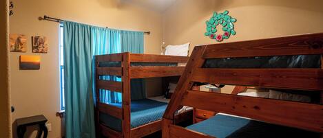A room with two bunk beds, a ceiling fan, a window with curtains, and a wall decoration.