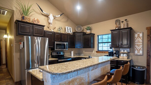 A modern kitchen with dark cabinets, stainless steel appliances, a granite countertop, and a stone island with bar stools.