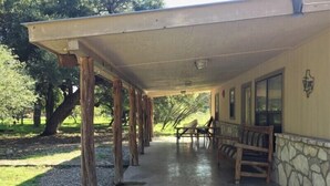 A covered outdoor seating area with stone walls and wooden pillars, featuring a bench and a table. - Pecan Acres - Cypress Bend Subdivision (Concan)