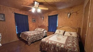 A room with two beds, wooden walls, a ceiling fan, and a rustic decor including a cow skull. - Pecan Acres - Cypress Bend Subdivision (Concan)