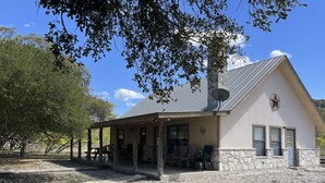 A two-story building with a stone foundation and a metal roof. There is a covered porch with outdoor seating. - Pecan Acres - Cypress Bend Subdivision (Concan)