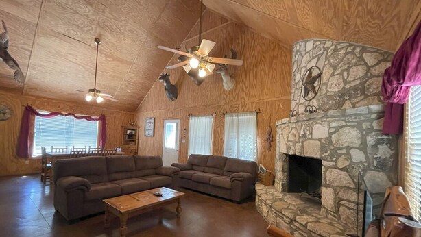 A cozy living room with a stone fireplace, wooden ceiling, and a large sofa. - Pecan Acres - Cypress Bend Subdivision (Concan)