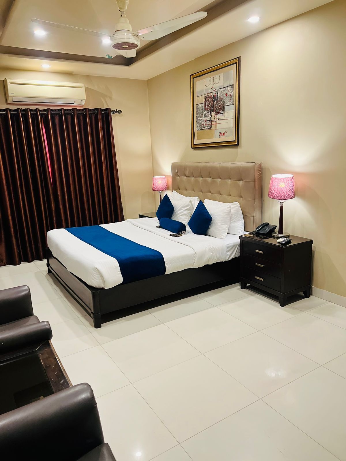 A neatly arranged bedroom with a bed, bedside tables, a ceiling fan, and a painting on the wall.