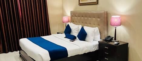 A neatly arranged bedroom with a bed, bedside tables, a ceiling fan, and a painting on the wall.
