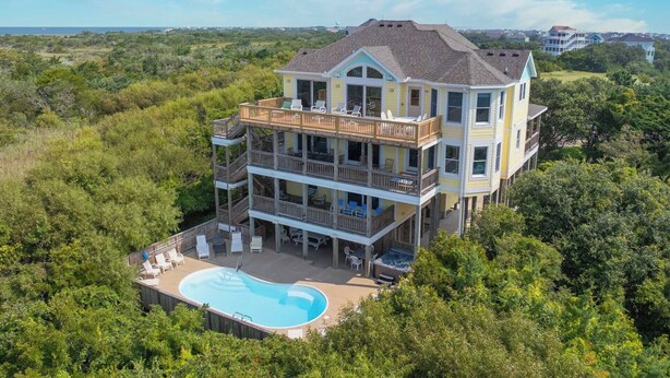 A multi-story house with a large deck and a swimming pool.