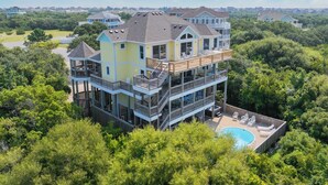 A multi-story house with a large deck, a swimming pool, and a view of the surrounding area.