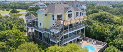 A multi-story house with a large deck, a swimming pool, and a view of the surrounding area.