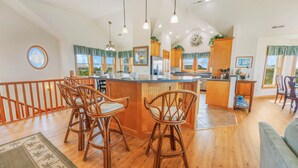 A spacious kitchen with a central island, wooden bar stools, and a view of the outdoors through large windows.