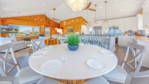 A modern kitchen with white cabinets, a blue backsplash, and a dining area with a round table and gray chairs. - Canalfront Dog Friendly Home w/ Hot Tub, Private Boat Ramp/Dock, Cargo Lift (Avon)