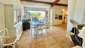 Una cocina amplia con armarios blancos, un comedor con una mesa redonda y sillas, y vistas al exterior a través de grandes puertas correderas de cristal.