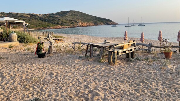 Un entorno de playa con mesa y sillas de madera, un paraguas rústico y una planta de cactus.