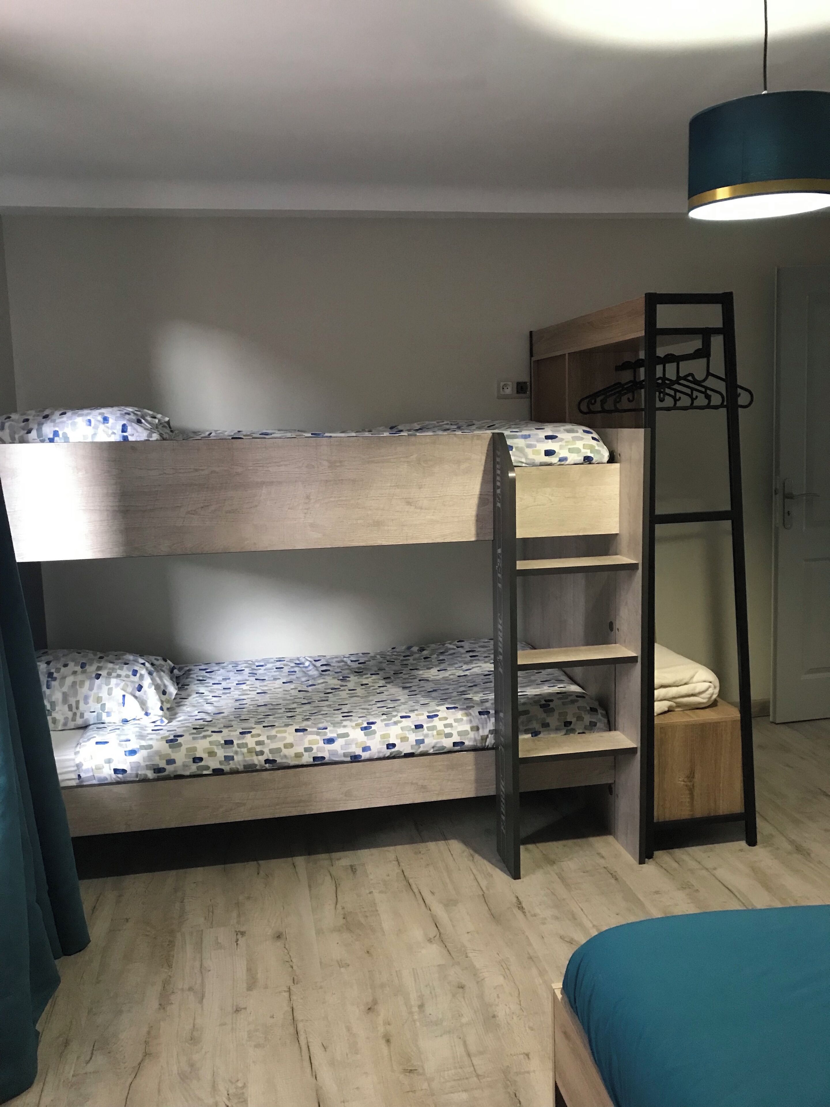 A bunk bed with a ladder, a small shelf unit, and a hanging light fixture.