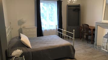 Ein Schlafzimmer mit einem Bett, einer Kommode, einem Schreibtisch, einem Stuhl, einer Heizung und einem Fenster mit Vorhängen.