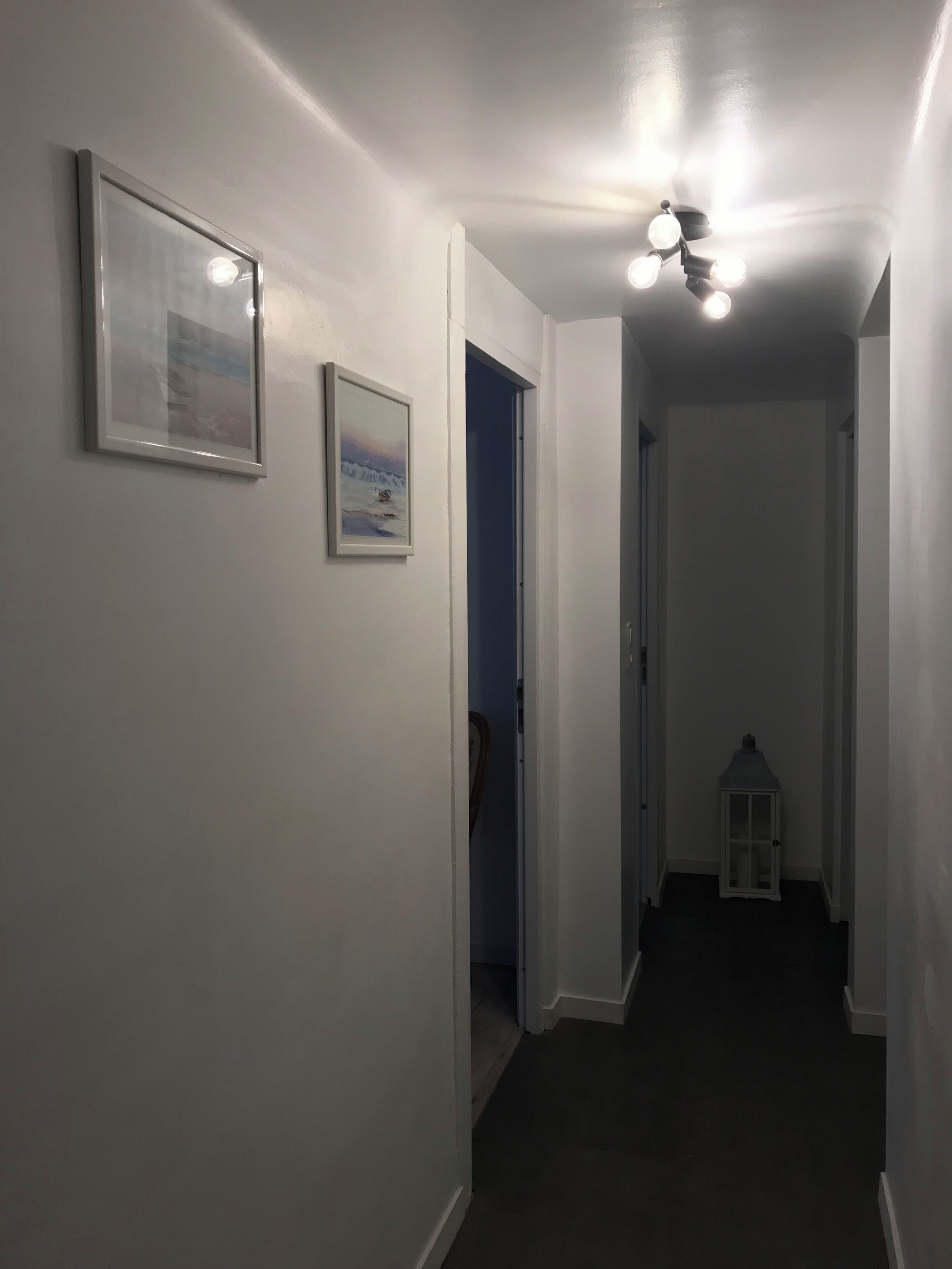 A hallway with white walls, a ceiling light fixture, and a small white lantern.