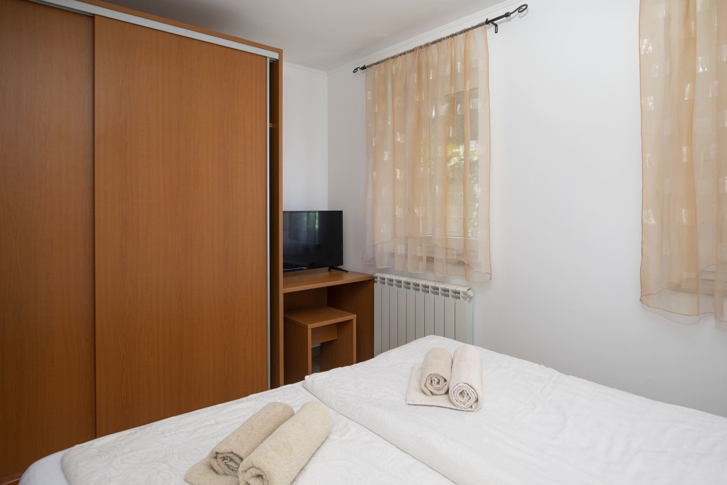 Une chambre d’hôtel équipée d’un lit, d’une télévision, d’une armoire et d’une fenêtre avec des rideaux légers.